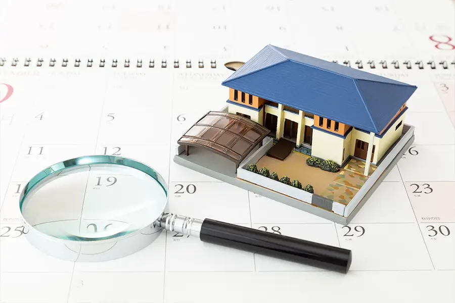 カレンダーの上に家の模型と虫眼鏡が置いてある 写真